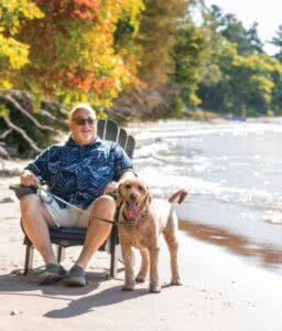 Man sitting in a beach chair next to water with a dog on a leash