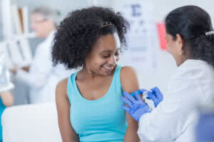 Female doctor places a bandage on teenage female patient's arm. The patient received an immunization in her arm.