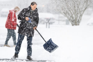 Young man and woman in winter coat cleaning shoveling driveway street from snow in heavy snowstorm