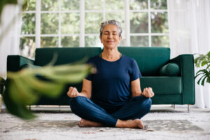 Senior woman meditating in lotus position at home.